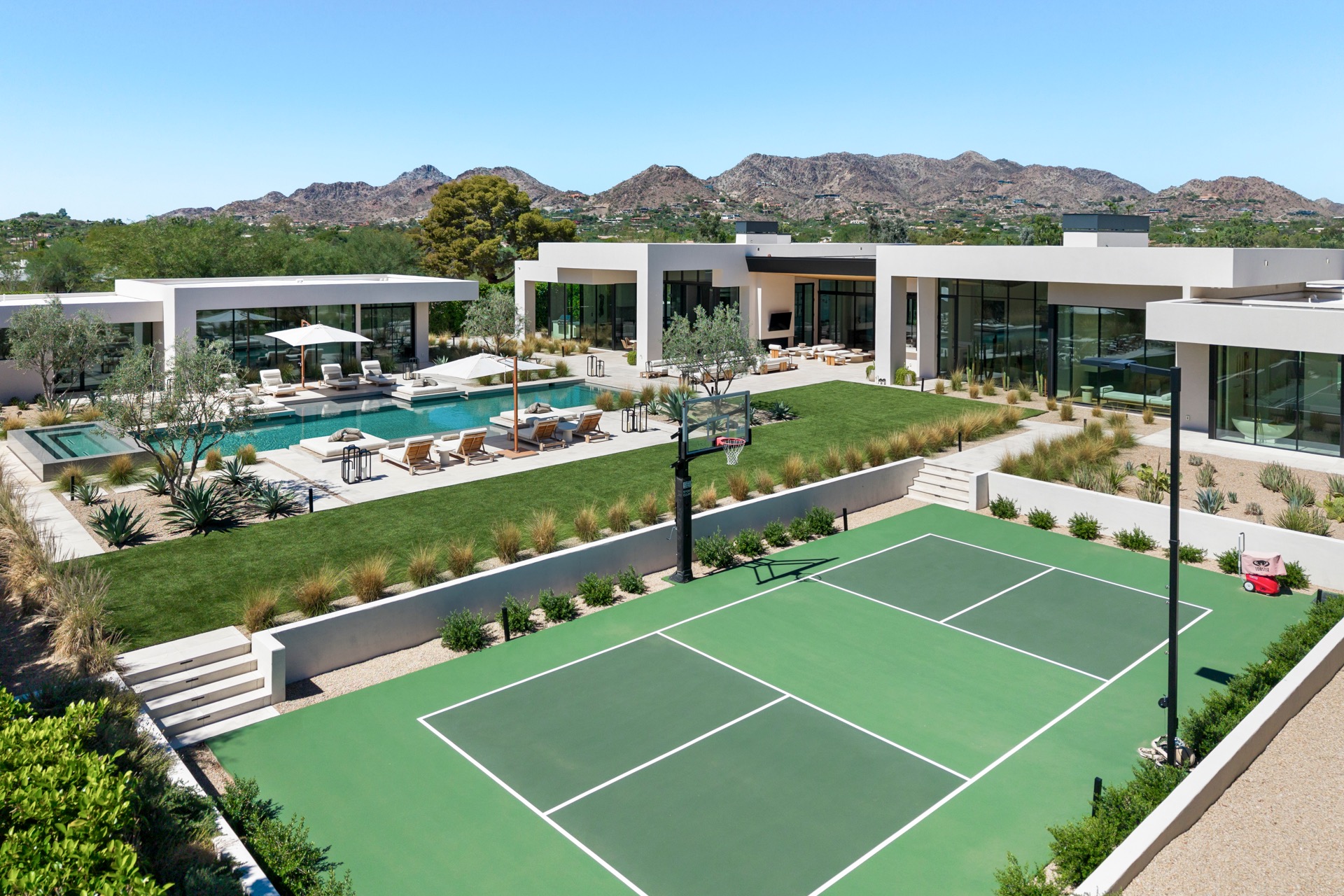 Modern luxury estate with a sports court, pool, landscaping, and desert mountain views